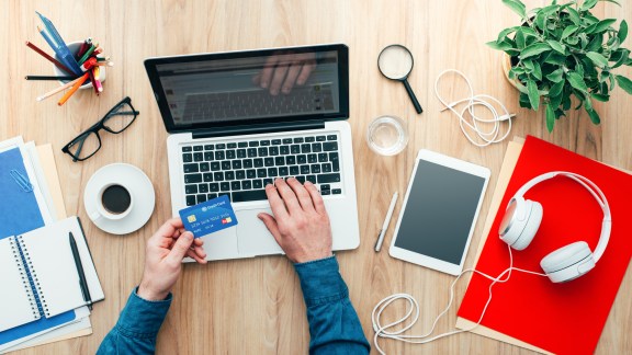 Man working at desk and purchasing products online, he is making a payment using a credit card, online shopping concept