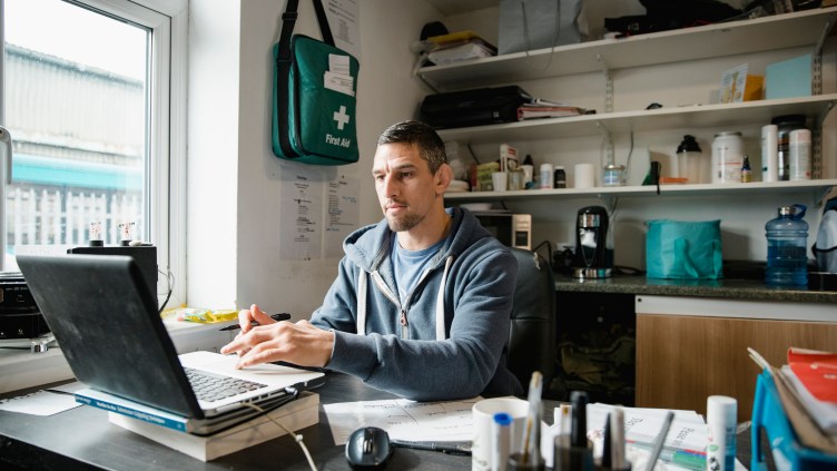 Mid-adult man is working on the laptop in his office, ordering new supplies for his gym.