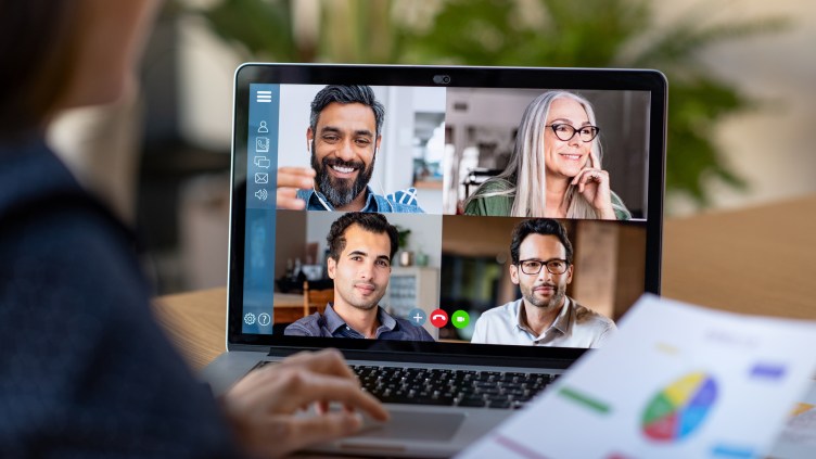 Back view of business woman talking to her colleagues about business plan in video conference. Multiethnic business team using laptop for a online meeting in video call. Group of businessmen and businesswomen smart working from home.