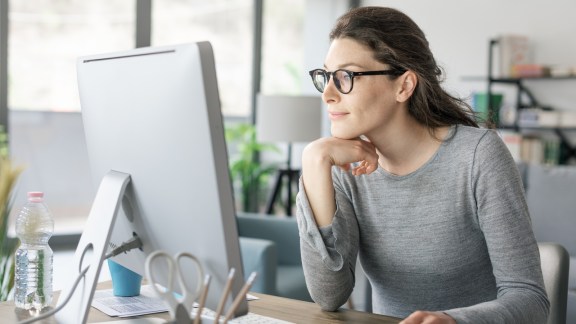 Professional woman sitting at desk and connecting with her computer, she is working from home