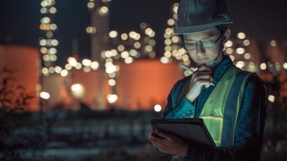 Engineer Petrochemical Asian man work late and hard with Smart tablet Inside the Refinery oil and gas Industry Factory at night