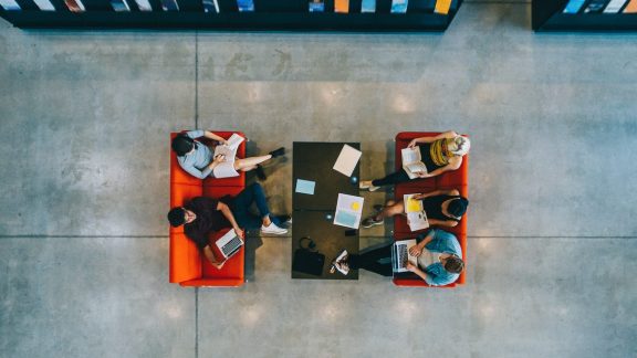 Top view of university students sitting in a library with books and laptop. Young people studying together at college library.