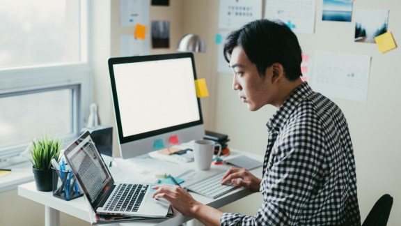 Man looking at computer code on a laptop while working from his small office.