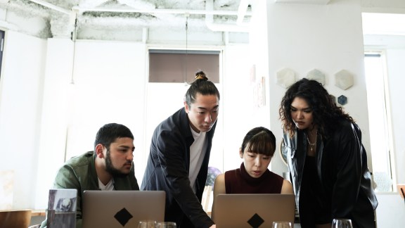 Group of colleagues talking together in coworking office and cafe.