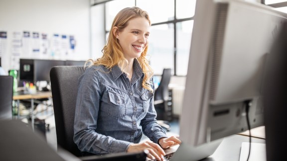 Smiling young woman sitting at her desk and working on laptop computer. Business woman using computer at her work place.