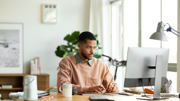 Male freelancer using desktop PC at desk. Young businessman is working at home office. He is in smart casual.