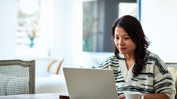 Mid adult woman in her 30s sitting at table and looking at computer, remote working, freelancer, small business