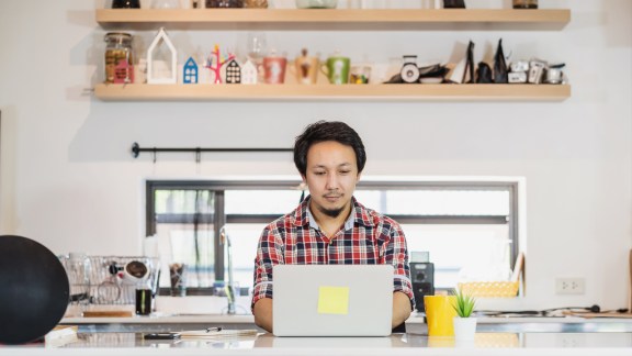 Working at home in Covid-19 pandemic concept, Asian man working at home with technology laptop and mobile phone at kitchen room