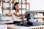 Happy woman working in bakery, pastry shop using tablet and cash computer