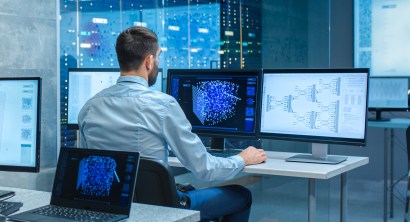 Beautiful Male Computer Engineer and Scientists Create Neural Network at His Workstation. Office is Full of Displays Showing 3D Representations of Neural Networks.