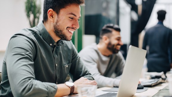 Smiling male colleagues working at desk in office