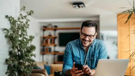 Portrait of a cheerful man using smart phone at home office.