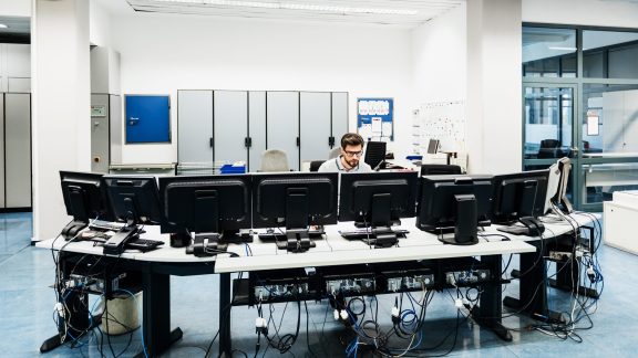 An engineer working at a desk with multiple computers in a printing factory control room.