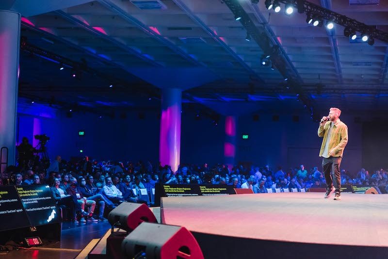 Man standing on stage speaking in front of an audience.